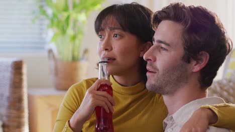 video of happy diverse couple drinking beer and talking in living room