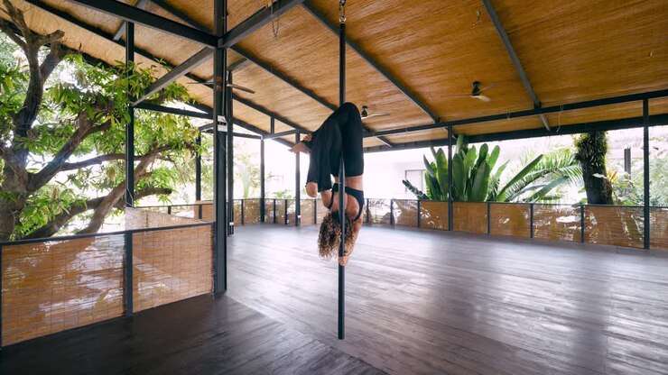 Donna che esegue eleganti acrobazie aeree al palo in uno studio tropicale