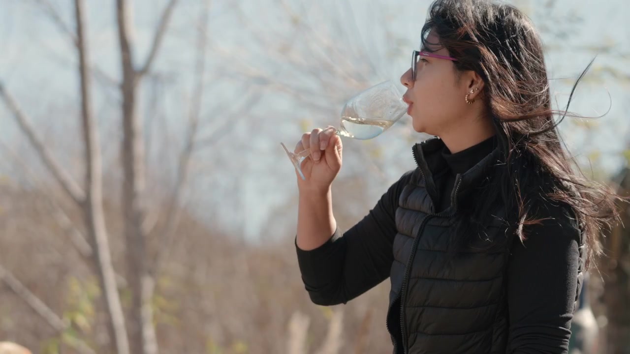 Woman drinking wine outdoors while enjoying a calm moment surrounded by trees and nature.
