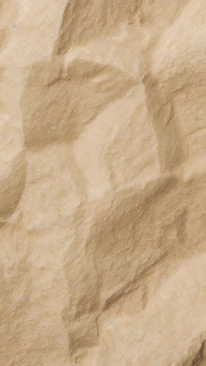 Vertical video: Panning camera revealing fold details at close range, beige crumpled paper