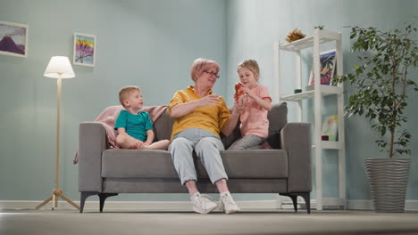 grandma shows piggy bank to girl while grandson sits on sofa