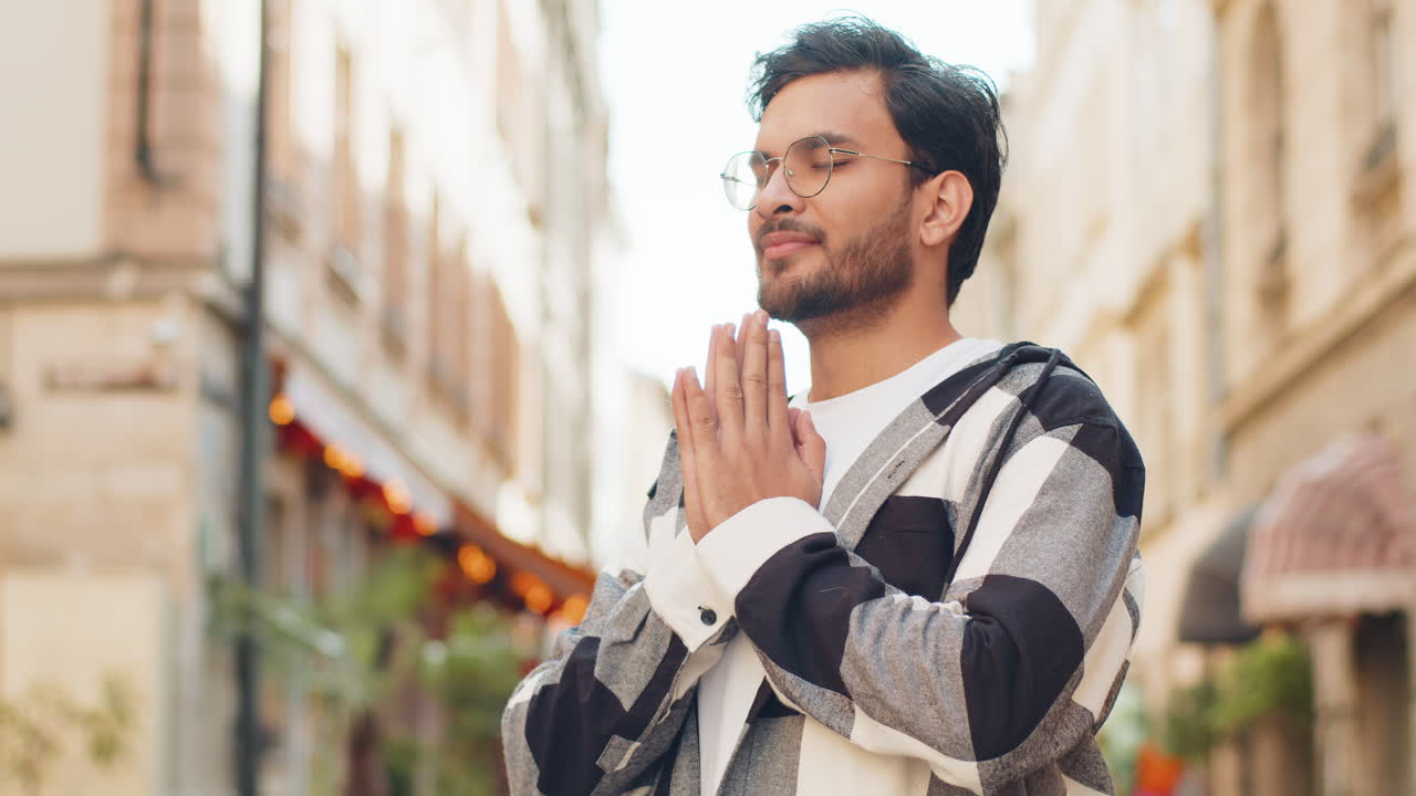 Religious indian man praying with closed eyes to god asking for blessing while standing on street