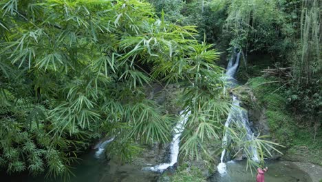 Ascending-aerial-view-of-a-young-lady-taking-a-selfie-at-the-base-of-a-waterfall-in-slowmotion