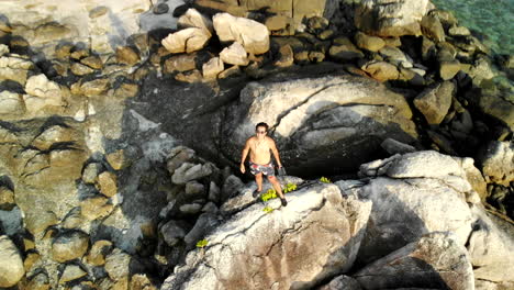 Aerial-shot-of-a-man-on-top-of-rocks-near-a-beach-with-clear-water-and-corals