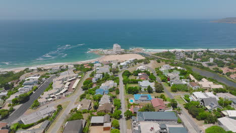 Aufsteigende-Luftaufnahmen-Von-Stadtbezirken-Hoch-über-Der-Meeresküste.-Sandstrand-Und-Meeresoberfläche-Im-Hintergrund.-Plettenberg-Bay,-Südafrika