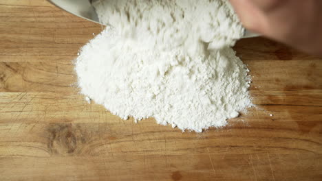 close up: chef pouring flour in a mound on a wooden table