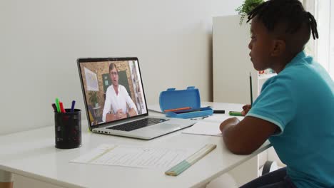 niño afroamericano sentado en un escritorio usando una computadora portátil teniendo una lección escolar en línea