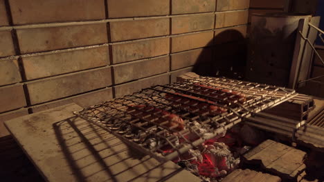 handheld shot of man flipping sausages in a grilling basket on a charcoal bbq at night