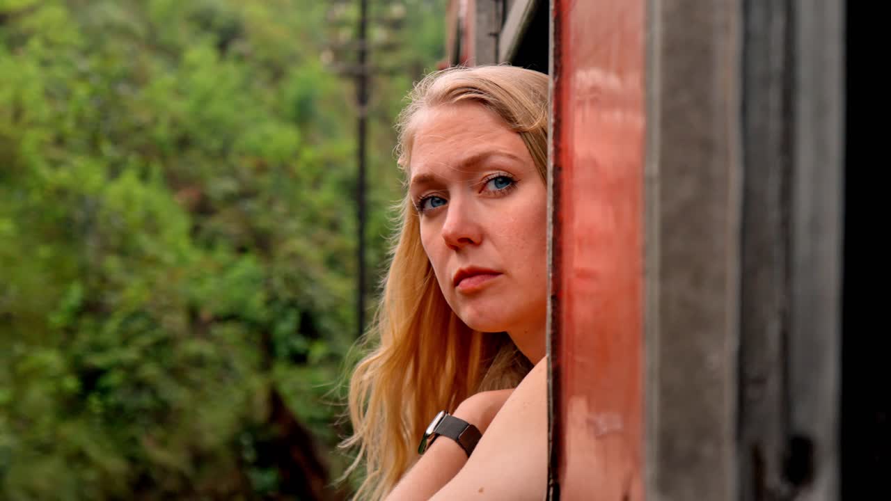 A young woman looks thoughtfully out the window of a moving train on the famous Ella to Kandy railway in Sri Lanka.