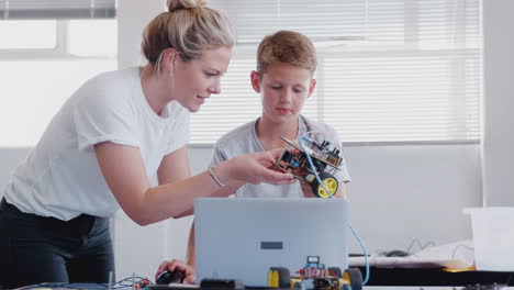 male student with teacher building robot vehicle in after school computer coding class