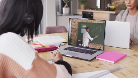 middle eastern teenage girl using laptop for video call, with male teacher on screen