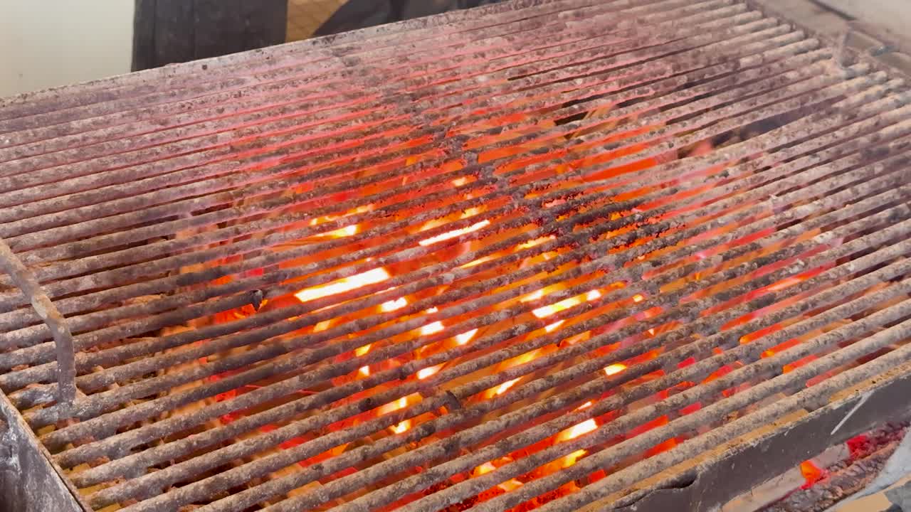 Inquadratura dall'alto di un intenso fuoco arancione e braci ardenti che bruciano sotto una griglia metallica.