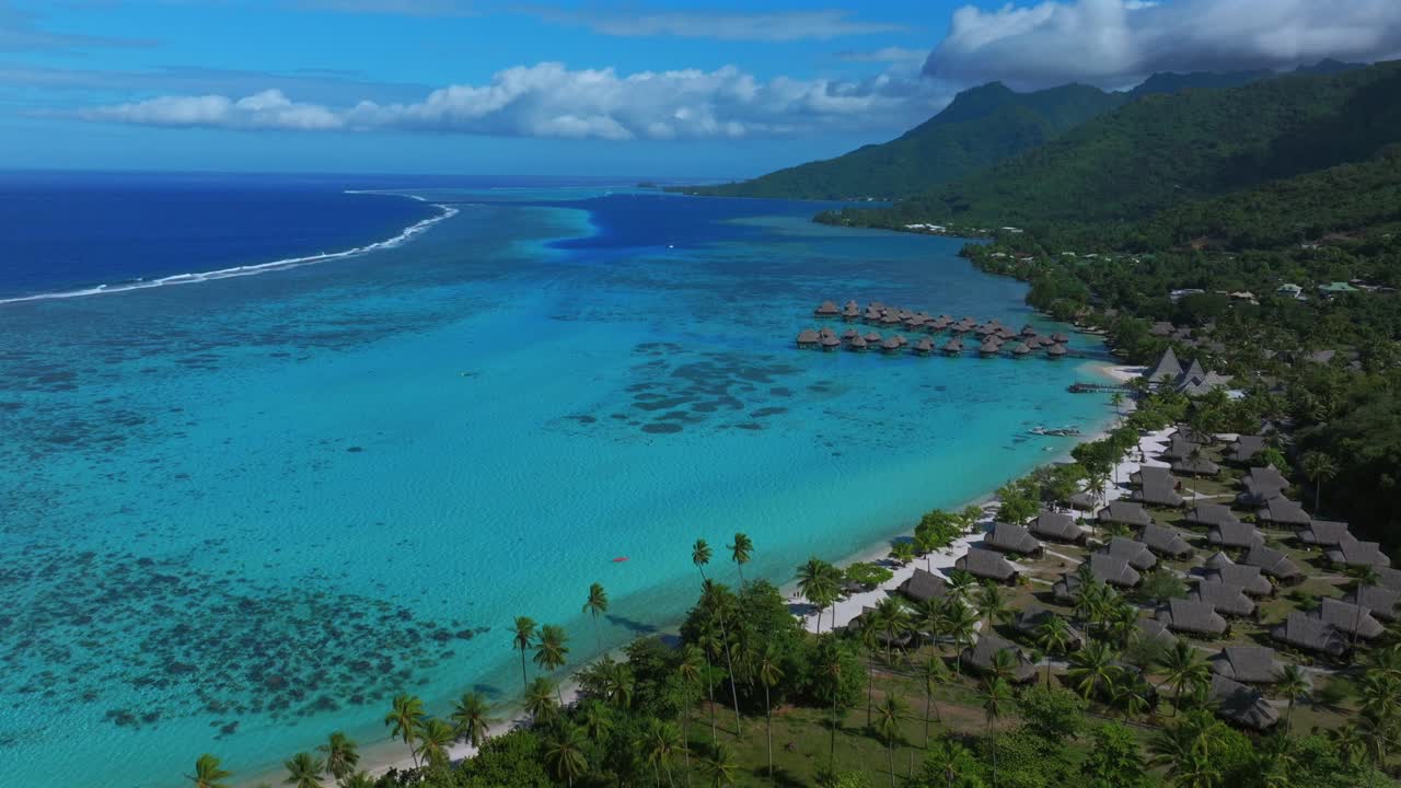 Tropisk ø i Stillehavet, Moorea Opunohu Bugt kystlinje. Offentlig strand, bungalows, motorbåd, Fransk Polynesien. Luftdroneoptagelse af koralrev, solrig morgen, blå himmel, skyer, turkis lagune, med dronebevægelse fremad og opad.