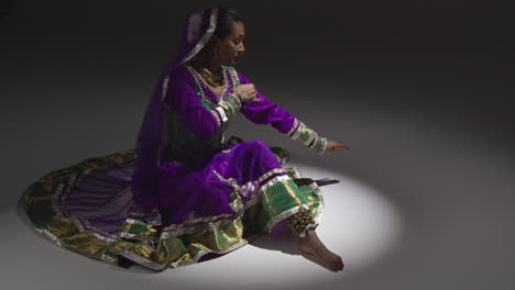 une danseuse de kathak exécutant une danse vêtue d'une robe indienne traditionnelle assise sur le sol sous les projecteurs