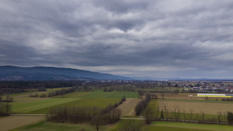 Aerial-hyper-lapse-of-rural-landscape-with-hedges,-meadows,-and-dramatic-cloudscape,-central-European-farming-landscape,-vicinity-of-Maribor,-Slovenia