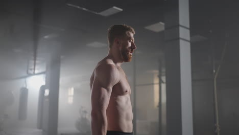 exhausted muscular man raises his head and looks into camera. he's covered in sweat and tries to catch a breath. exhausted male athlete is resting after training workout in gym