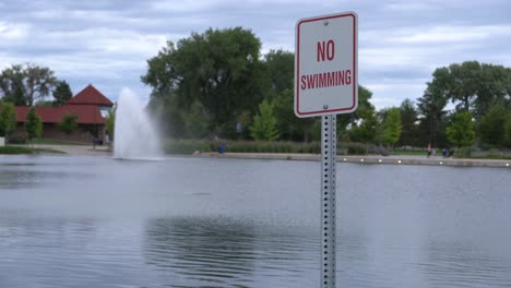 no swimming sign next to pond with fountain in background.