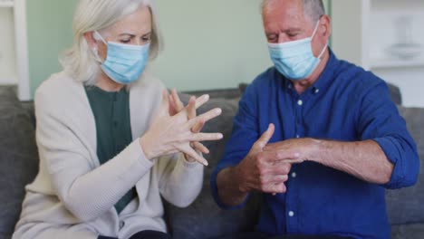 senior caucasian couple wearing face masks at home sitting on sofa