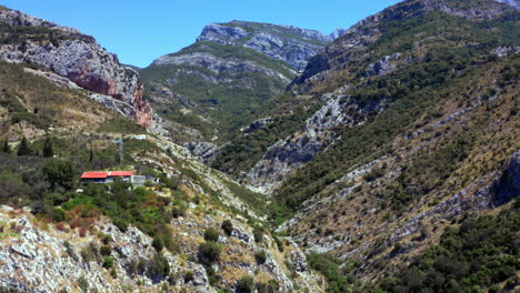 cresta de la montaña rocosa cerca de la ciudad de stari bar, montenegro, con árboles y arbustos que cubren la empinada ladera seca de la montaña, acantilados y colinas sobre el desfiladero, casas con tejados rojos y postes de servicios públicos a la izquierda