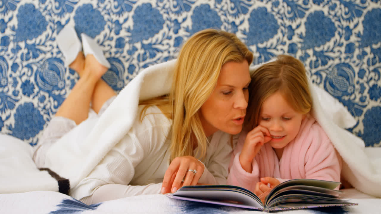 vista frontal de una joven madre y hija caucásicas mirando un álbum de fotos en la cama en casa 4k