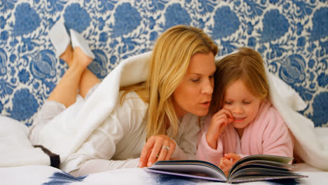 Front-view-of-young-Caucasian-mother-and-daughter-looking-at-photo-album-on-bed-at-home-4k