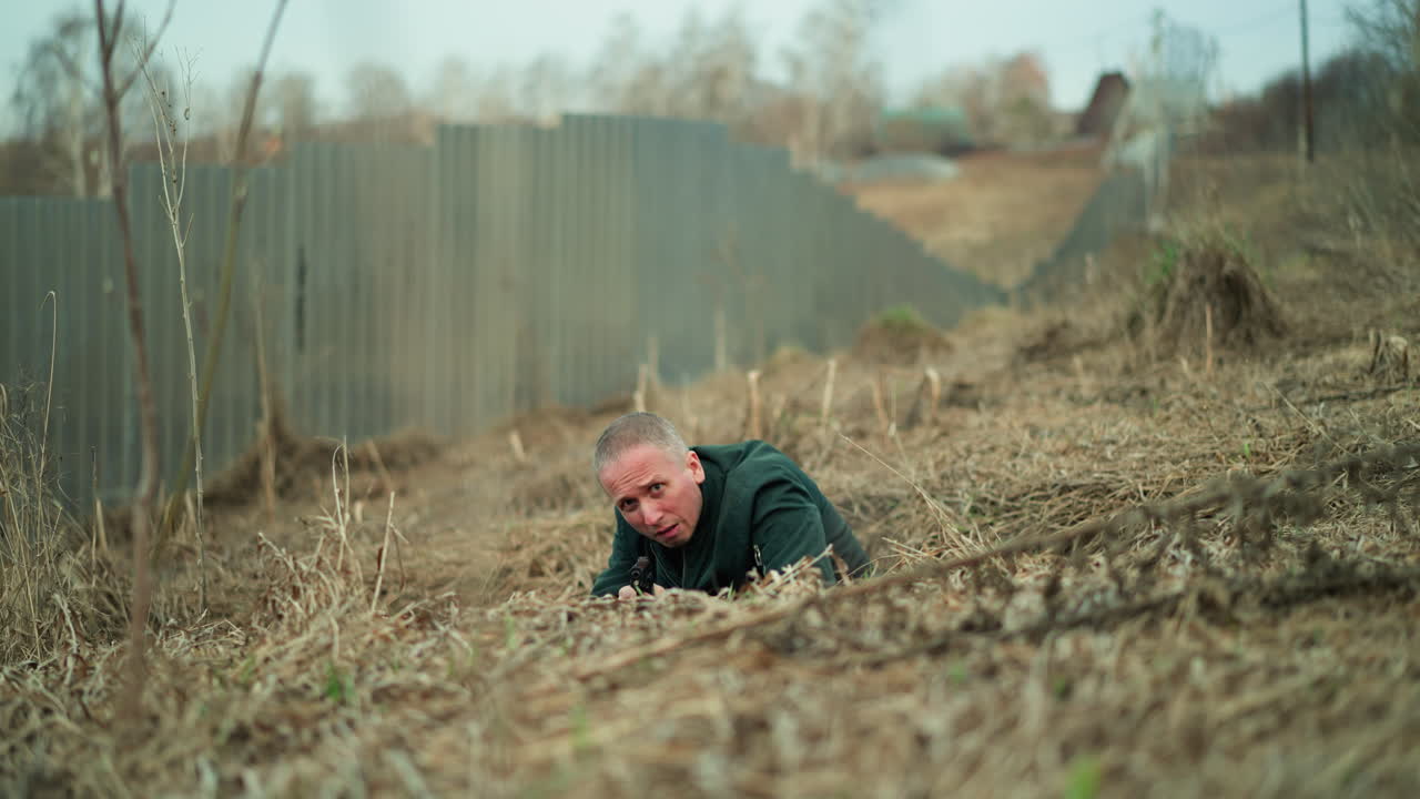 건조한 잔디를 통해 기어가는 남자의 가까운 시각, 권총을 들고, 그는 녹색 재을 입고 있으며 전술적인 상황에있는 것처럼 보입니다.