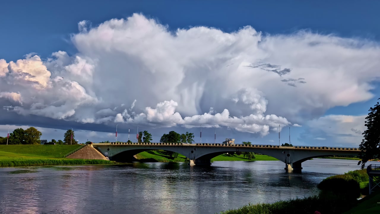 Majestic clouds over a serene river with a stone bridge in daylight