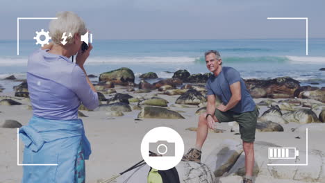 pantalla de la interfaz de la cámara del teléfono inteligente sobre feliz pareja de ancianos caucásicos junto al mar tomando fotos