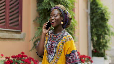 Mujer-Joven-Y-Guapa-Con-Ropa-Tradicional-Hablando-Por-Teléfono-Alegremente-En-El-Bonito-Patio-Con-Flores