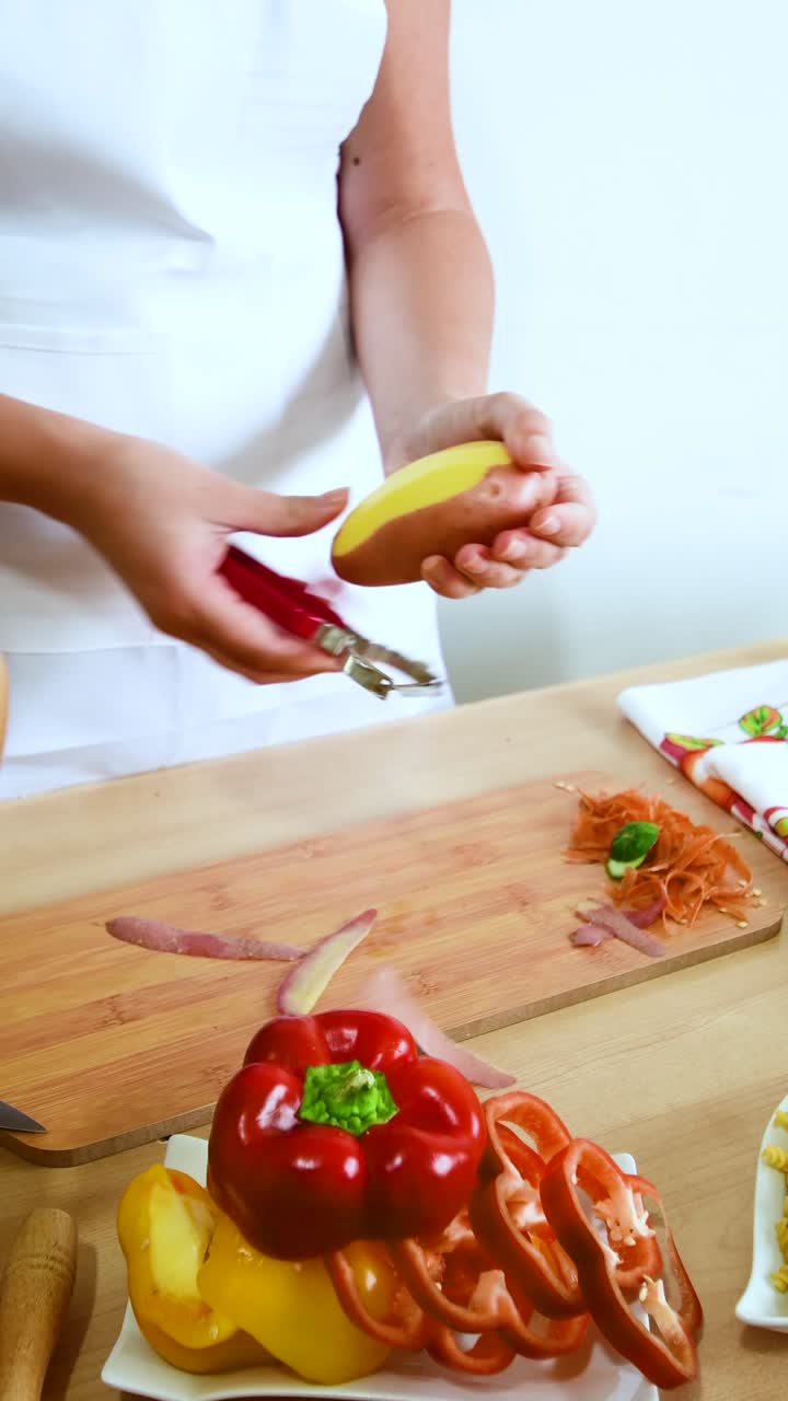 Female hand, cook peeling potatoes on the wooden table.