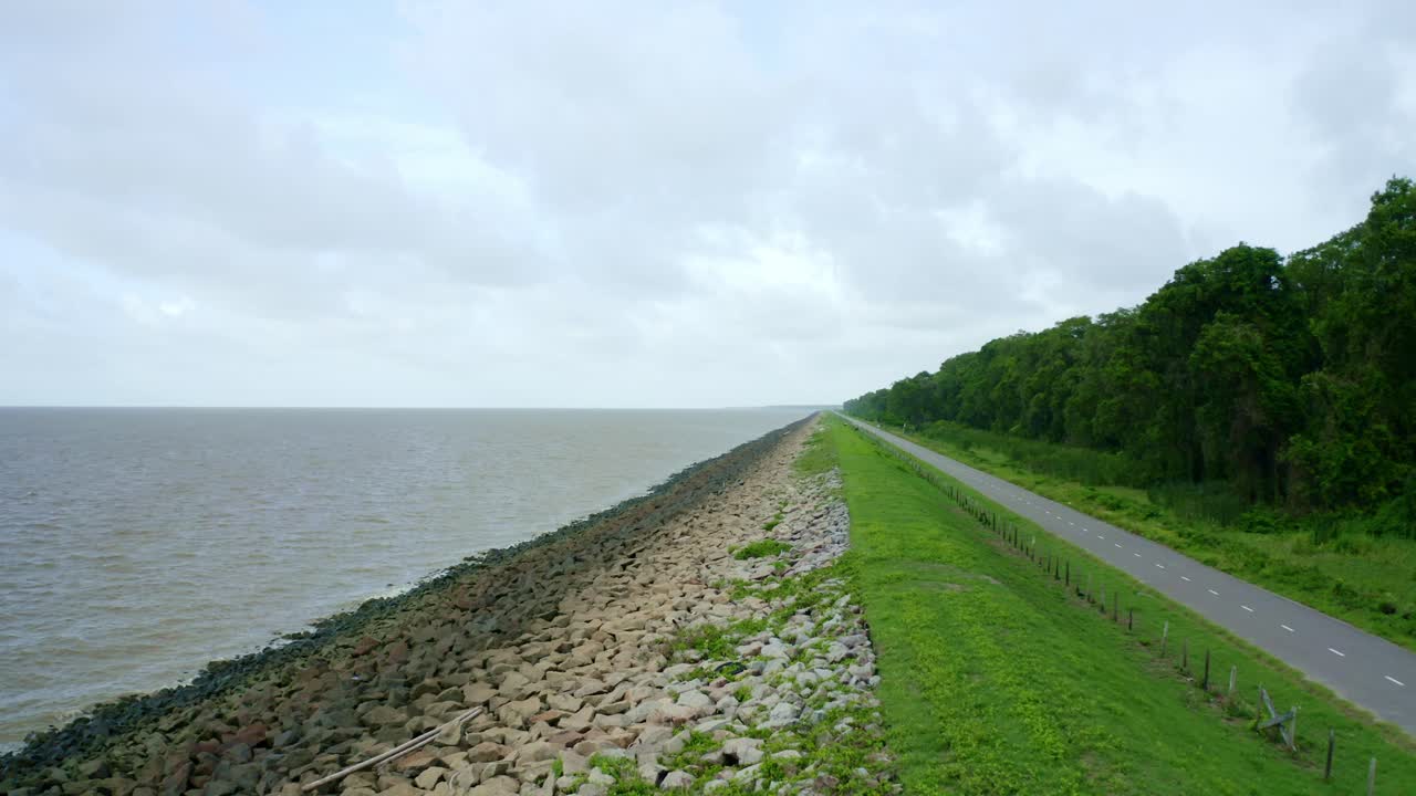 Letecký pohled: Pohled na mořskou hráz podél asfaltové silnice, dron letící pozpátku, Severní Atlantický oceán a Nickerie Surinam