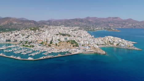 Drone-shot-over-the-marina,-seaside-boulevard,-beaches,-summer-in-Agios-Nikolaos-Crete-Greece