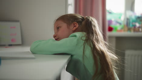 sad little girl rests while doing homework at desk in room