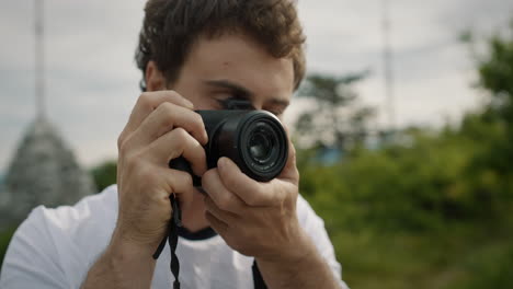 close up of a young man holding a camera, taking a picture and than taking a look without the camera