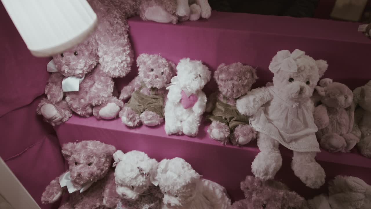 Morbidi orsetti di peluche rosa e bianchi sono disposti in modo ravvicinato su scaffali rosa, creando un'esposizione di giocattoli in un festoso stand del mercato.