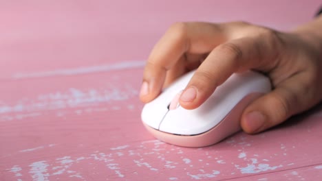 mano sosteniendo un ratón de computadora inalámbrico rosa en una mesa de madera rosa