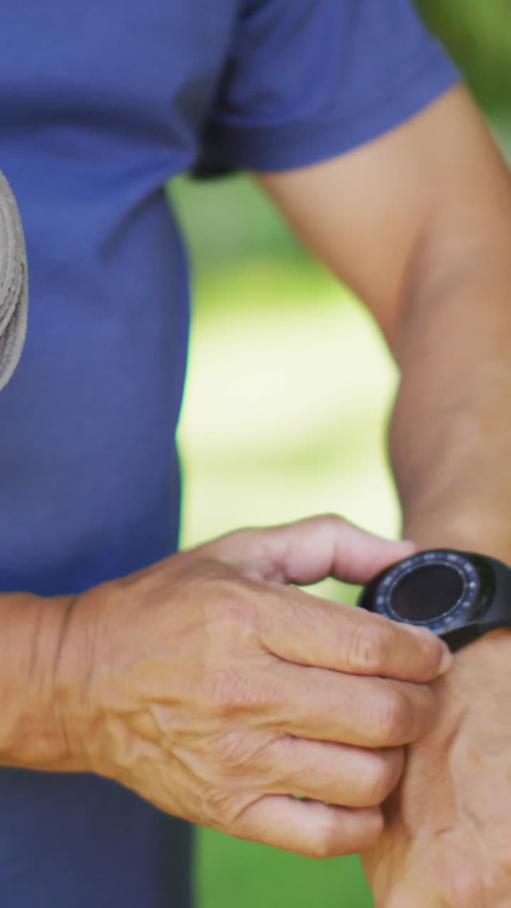 Video of midsection of biracial senior man holding yoga mat and checking smartwatch