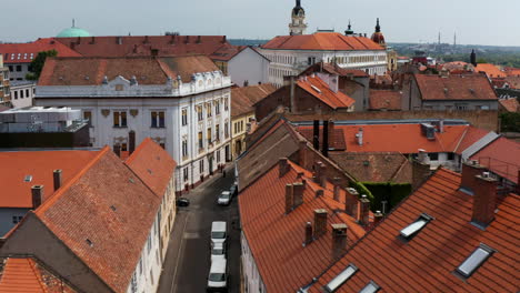 Am-Straßenrand-Von-Straßen-Zwischen-Rot-überdachten-Gebäuden-In-Pecs,-Ungarn,-Geparkte-Fahrzeuge