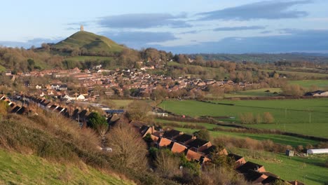 a landscape view of red brick houses, green fields and the historic tor monument in rural countryside town of glastonbury, england