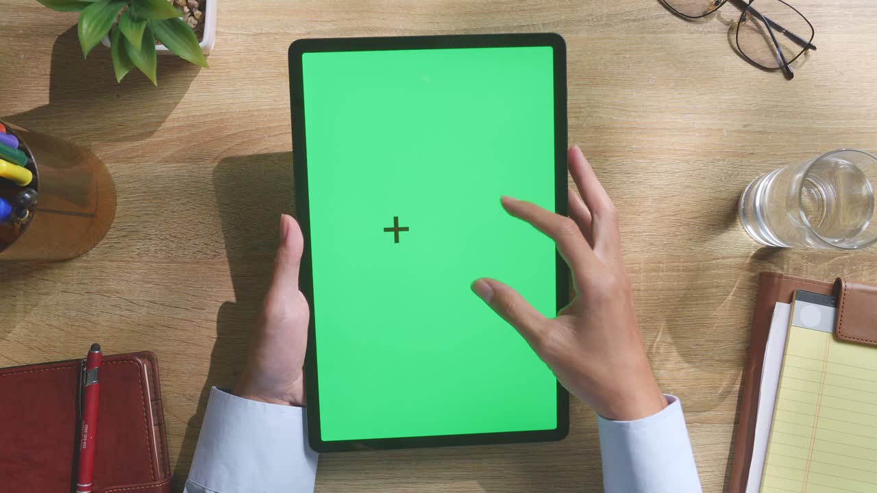 vista de arriba hacia abajo de una computadora portátil con pantalla verde simulada pantalla chromakey en un escritorio de oficina de madera al lado de la libreta con bolígrafos, gafas y un vaso de agua.