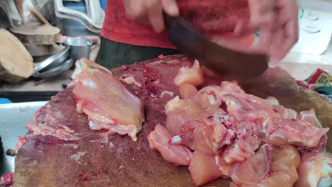 il macellaio sta tagliando il pollo con un coltello su una tavola di legno o un blocco di macellaio di legno