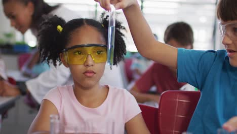 escolares de diversas razas con gafas protectoras sosteniendo un tubo de ensayo durante la clase de química