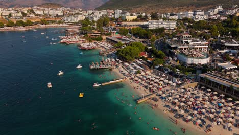 a crowded ksamil beach with turquoise water and many tourists enjoying the sun, aerial view