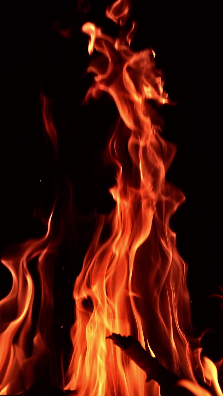 Bastoni di legno che bruciano in un grande falò. Lunghe lingue di fiamma che si estendono in alto nell'aria. Sfondo nero. Video verticale