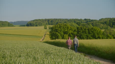 two farmers walk along a dirt road in rural landscape