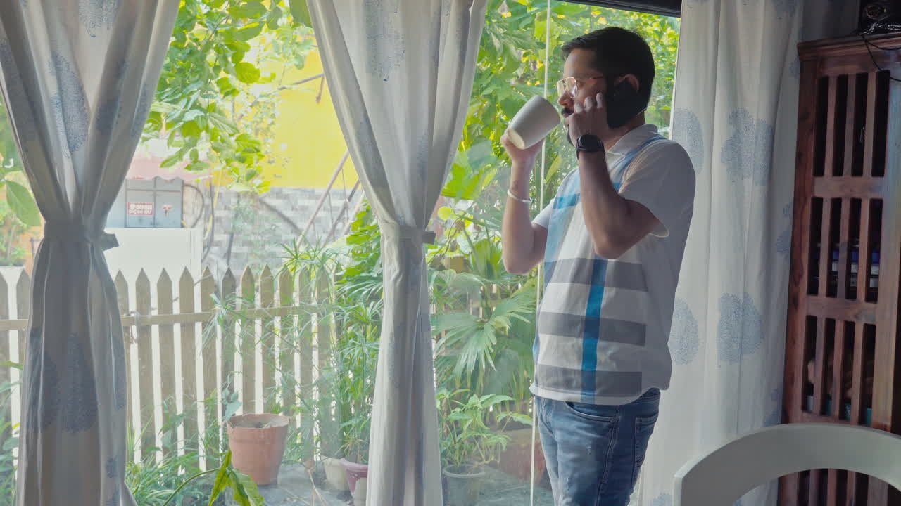 Man on a phone call with coffee in hand, looking through the window