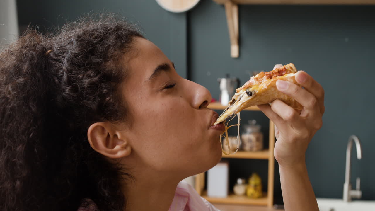 Young woman enjoying a delicious slice of pizza with a long cheese pull