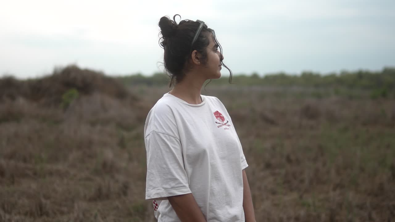 Giovane donna con una camicia bianca in piedi in un campo erboso, che guarda di lato