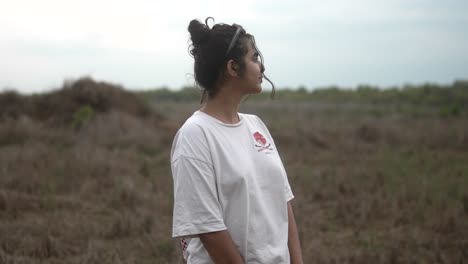 Young-woman-in-a-white-shirt-standing-in-a-grassy-field,-looking-to-the-side