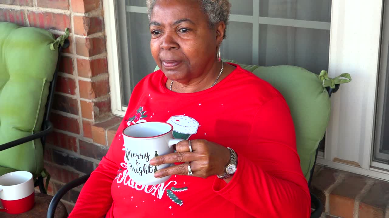 쌀쌀한 겨울날 데크에 앉아 뜨거운 김이 나는 차나 커피 컵을 들고 있는 행복한 성숙한 흑인 여성